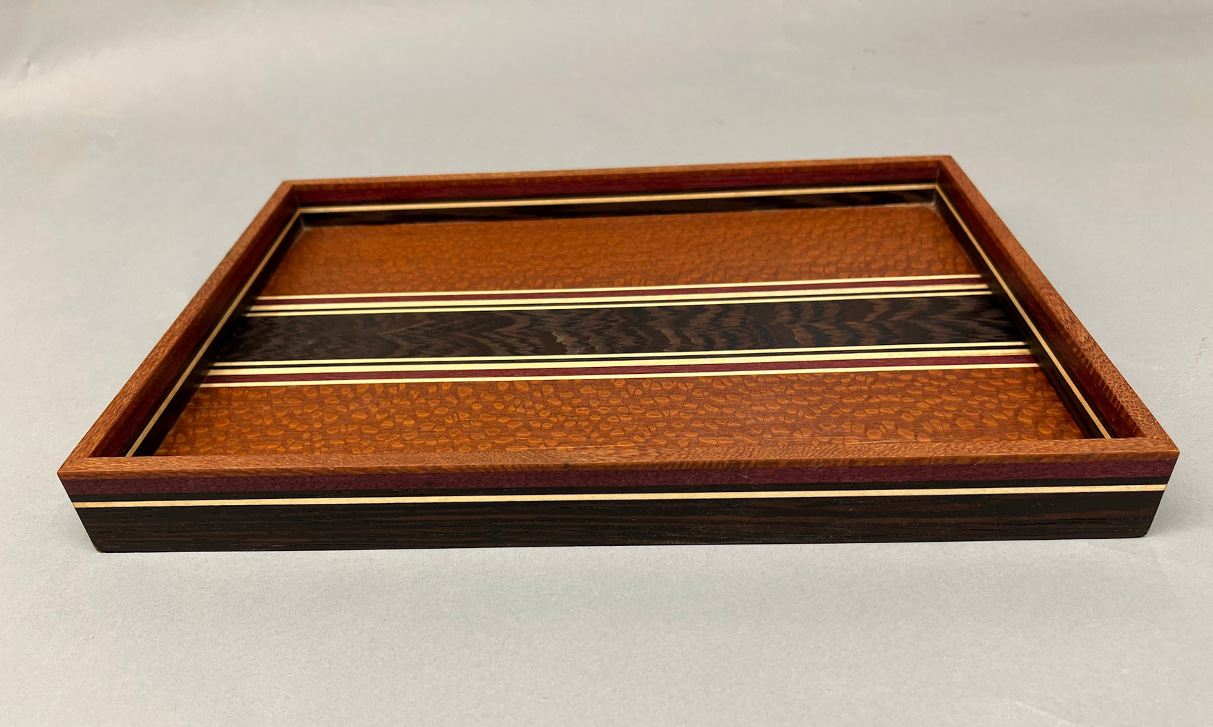 Lacewood, Wenge, Prupleheart and Maple wood tray. Finshed in Tung oil - naturally water resistant.