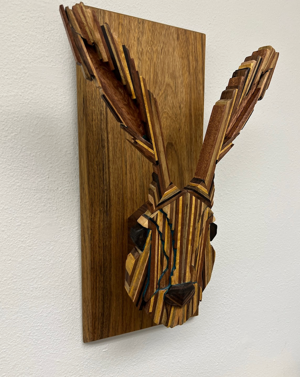 Rabbit head sculpture. Maple, Padauk, Lacewood, Movingia, Peruvian Walnut, Wenge, Black Limba, Iroko, Shedua woods, mounted on Shedua. Elevations of face highlighted by powdered Lapis Lazuli and blue tint epoxy.