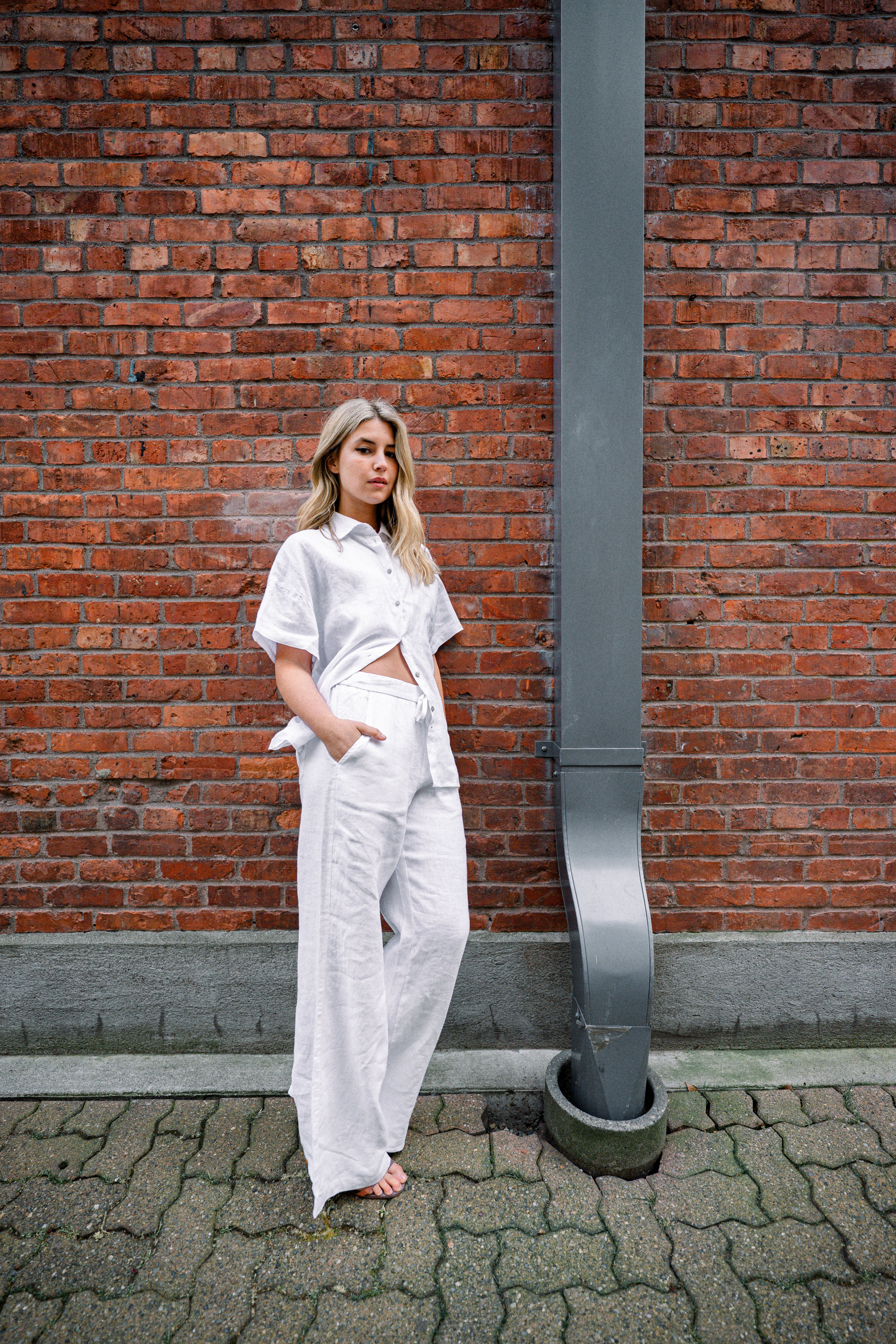 Woman in white outfit standing against a brick wall